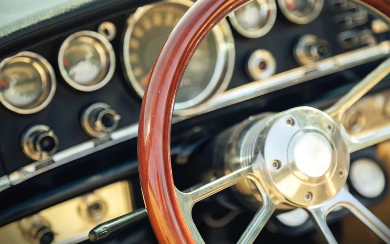 Interior de un coche clásico con volante de madera y salpicadero de cuero.